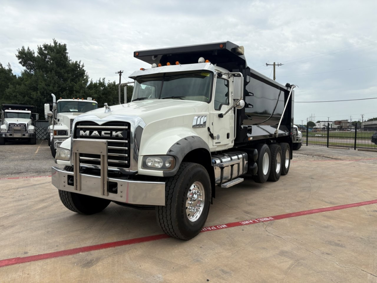 Dump truck with Mack grille showing front view of a 2020 Mack GR64F dump truck, white cab, black dump bed, multiple wheels, stock number B3427P.