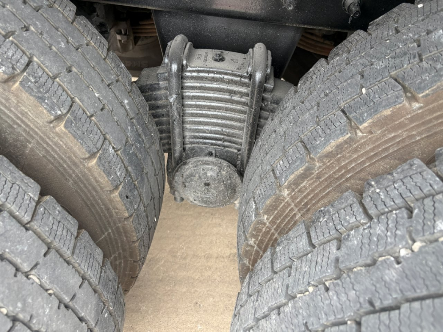 Axle differential and dual rear tires of a Mack GR64F truck seen from below, center-view shows driveshaft housing and suspension.