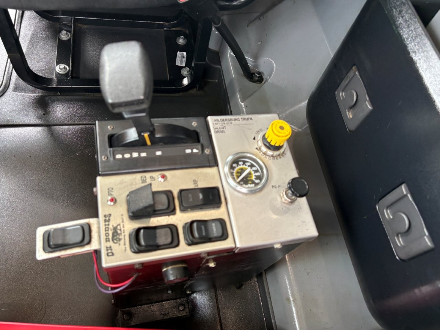Truck cab interior showing gear shifter and dash controls with yellow knob and gauge. Includes brake/throttle area and control switches.