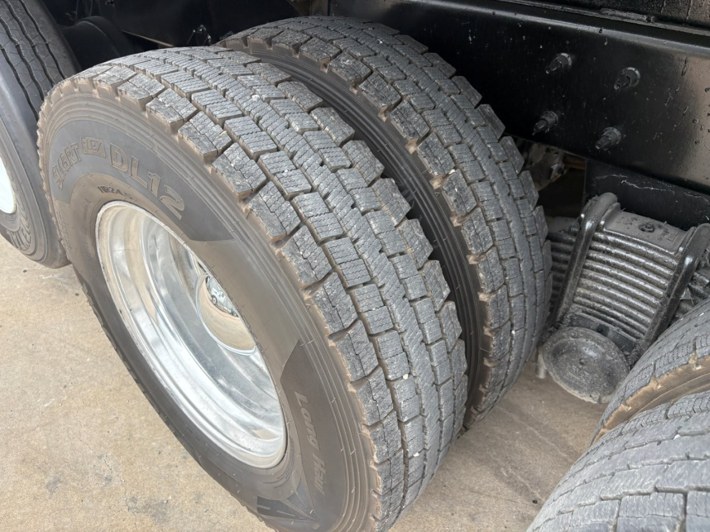 Truck rear dual tires and suspension showing dual rear wheels and leaf spring; tire tread and rim visible.