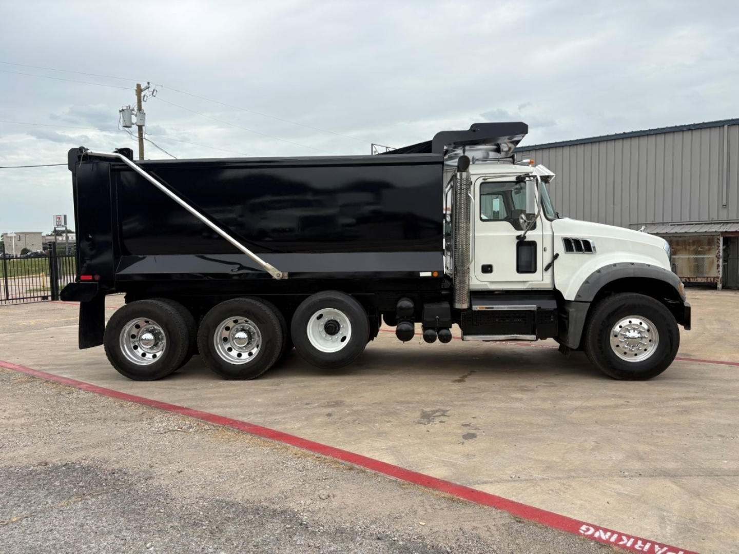 Dump truck side view showing 2020 Mack GR64F with black dump bed and white cab, six wheels, and hydraulic bed cover.