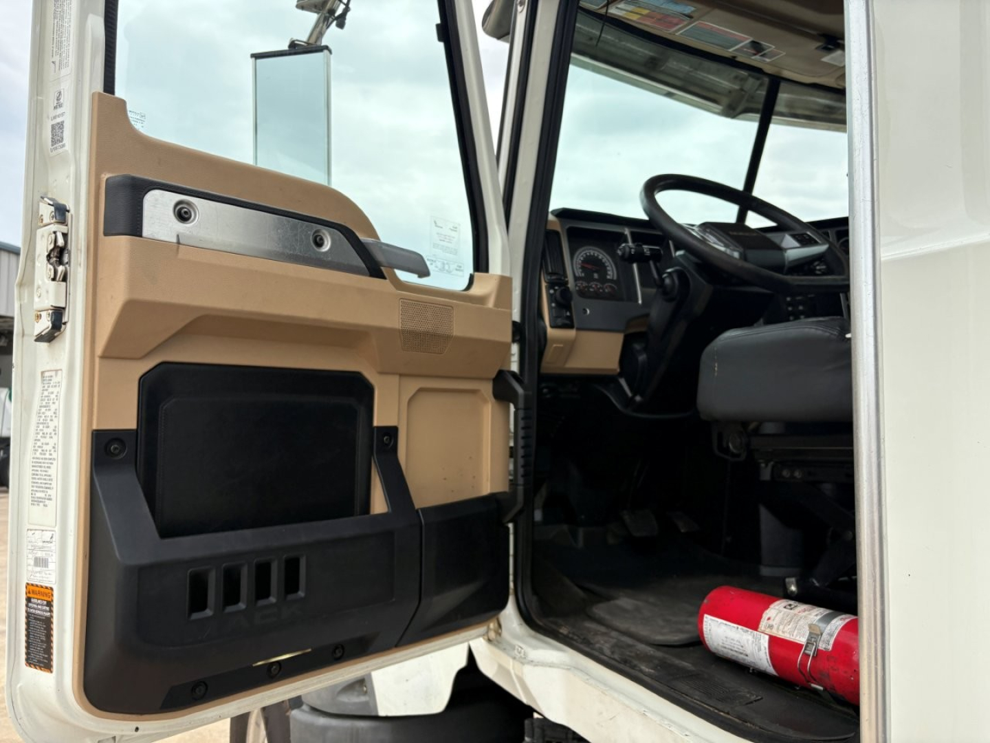 Truck cab interior visible through open door of 2020 Mack GR64F dump truck showing steering wheel dash and seat in first-person view.