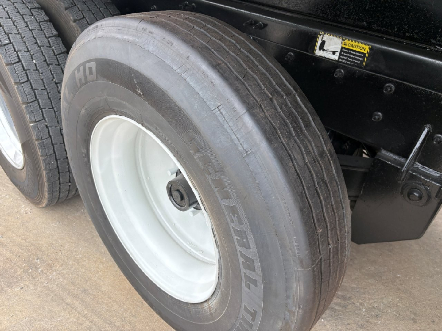 Mack GR64F dump truck wheel showing Goodyear tire and white rim with chassis frame and caution sticker nearby.