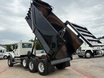 Dump truck in-service 2020 Mack GR64F with its dump bed raised, side view showing rear wheels and hydraulics.