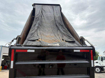 Dump truck bed of a 2020 Mack GR64F with tarp-covered dump box seen from rear, flat tailgate, black finish, and reflective safety markings.
