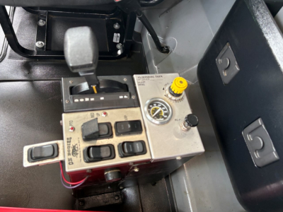 Truck cab interior showing gear shifter and dash controls with yellow knob and gauge. Includes brake/throttle area and control switches.