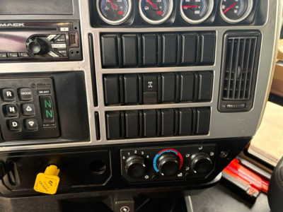 Mack GR64F dash panel showing gauges and controls including gear selector and climate controls, with yellow hood pin visible