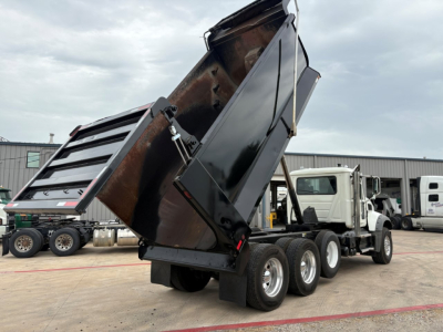 Truck with a raised dump bed, rear view showing triple axles and dump hydraulics.