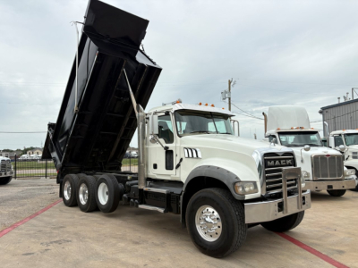 Dump truck in service showing raised dump bed on a Mack GR64F with tandem rear axles and chrome grille.