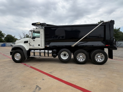 Dump truck side view showing Mack GR64F dump bed with black sides, white cab, three rear axles, chrome wheels, and hydraulic hoist. No visible text legible on the truck body.
