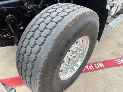 Mack GR64F wheel and tire close-up showing dual rear axle with heavy-duty tread and chrome wheel, part of dump truck chassis. Visible tire brand and wheel hardware.