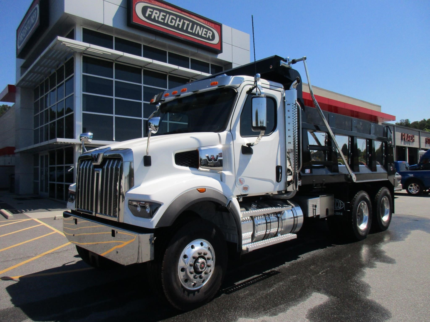 Western Star 47X dump truck in dealership lot, front three-quarter view with chrome grille, dual rear axles, and dump bed.