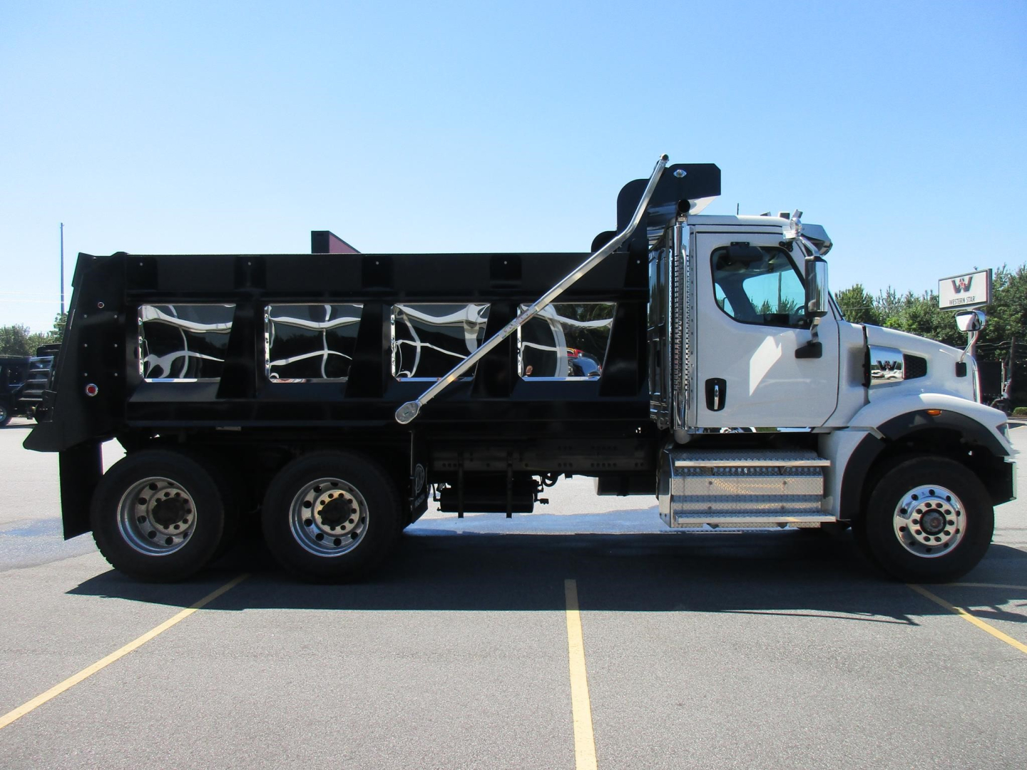 Dump truck side view showing a white cab and black dump bed with hydraulic support struts; wheel set has six tires on the chassis.