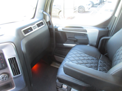 Truck cab interior showing front passenger seat with diamond stitching and black upholstery; door panel, dashboard vents, and floor illuminated by red ambient light.