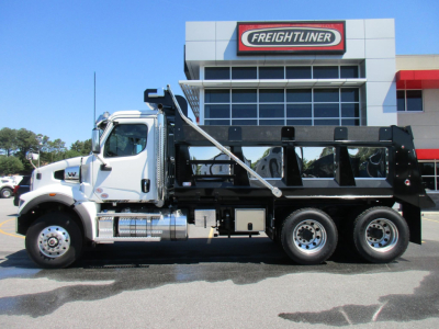 Western Star 47X dump truck side view with white cab and black dump body in front of Freightliner dealer building.
