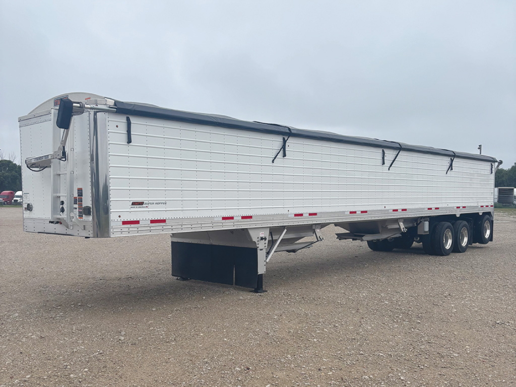 Timpte Super Hopper trailer in a field showing side view with tarpaulin cover and landing gear. Visible text includes model details and reflective tape along the sides.