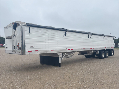 Timpte Super Hopper trailer in a field showing side view with tarpaulin cover and landing gear. Visible text includes model details and reflective tape along the sides.