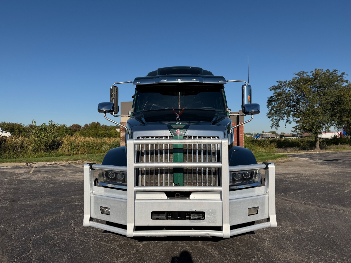 Conventional sleeper truck front view showing large chrome grille, bumper guard, and Western Star emblem; 2017 Western Star 5700XE in blue with green tie strap on grille.