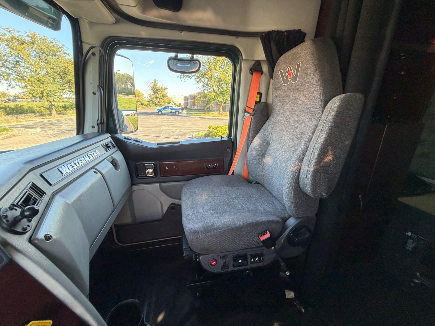 Inside cab of a 2017 Western Star 5700XE with grey fabric driver seat, steering wheel, dashboard, and large side window view.