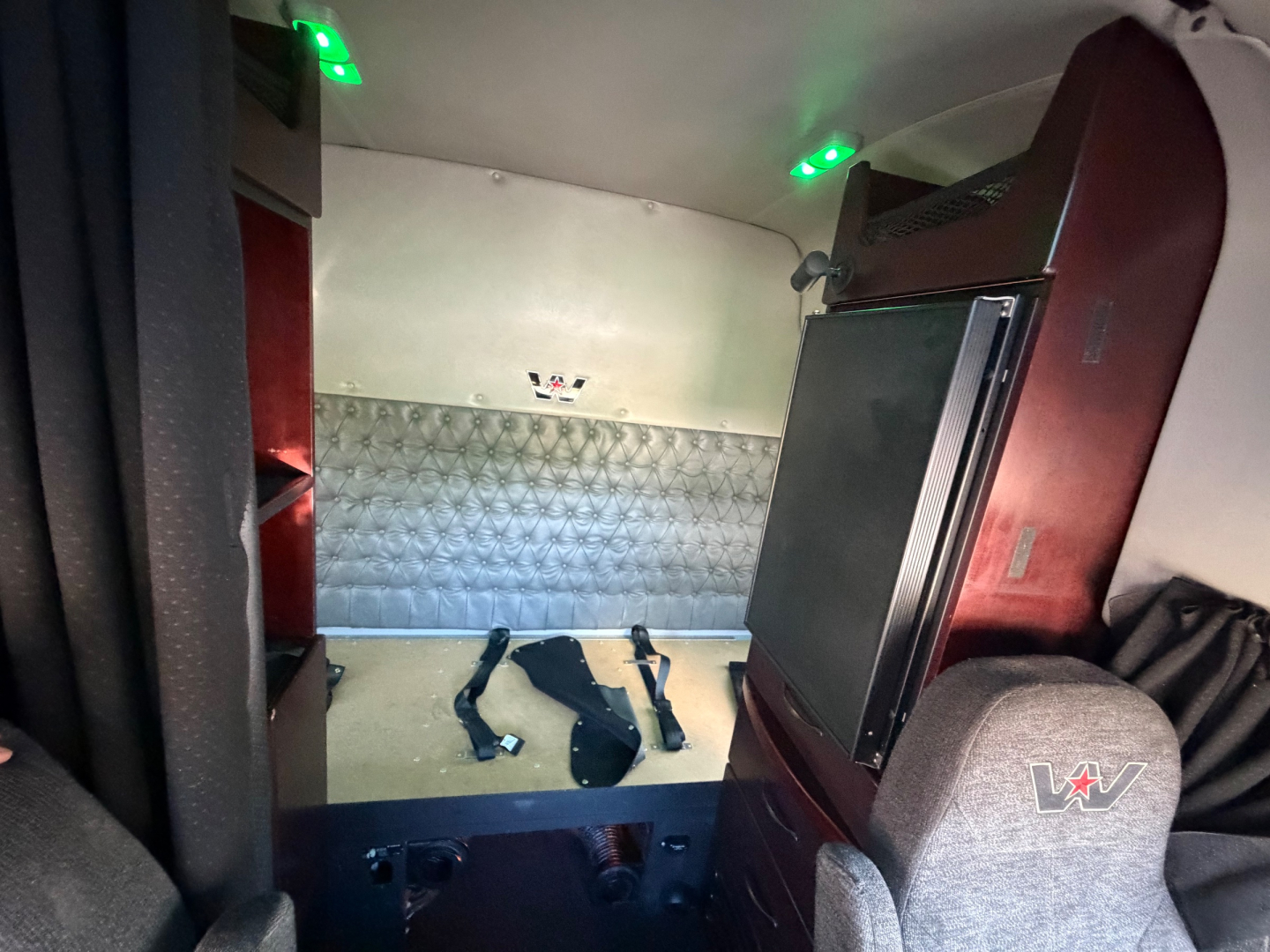 Interior cab of a 2017 Western Star 5700XE showing sleeper area with quilted metal side panel, overhead green indicator lights, and seats with 'W' logo.