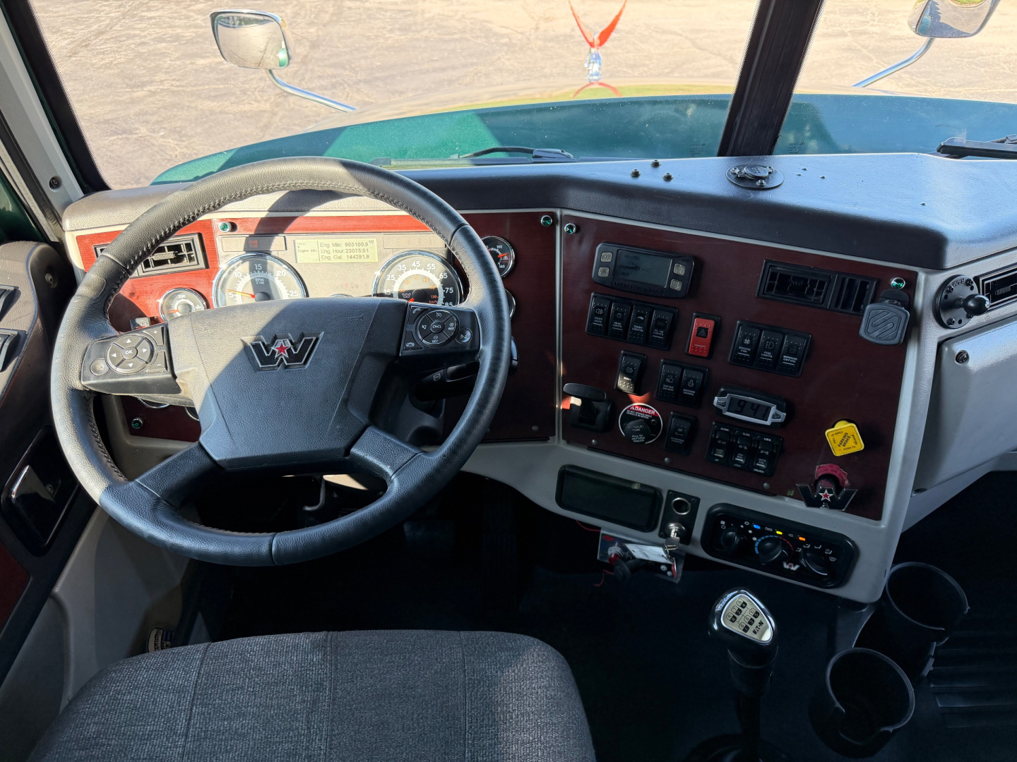 Conventional sleeper truck cab interior showing steering wheel and dashboard with gauges and control switches.