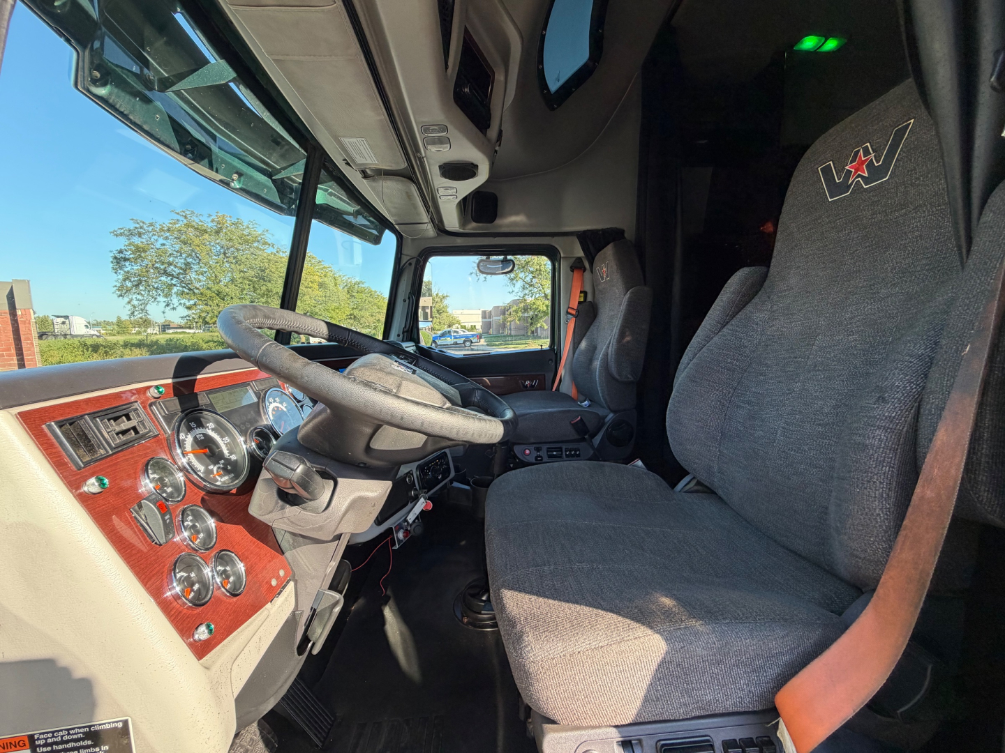Interior cabin of a 2017 Western Star 5700XE showing steering wheel, dashboard with gauges, driver seat, and upholstery with red woodgrain trim.