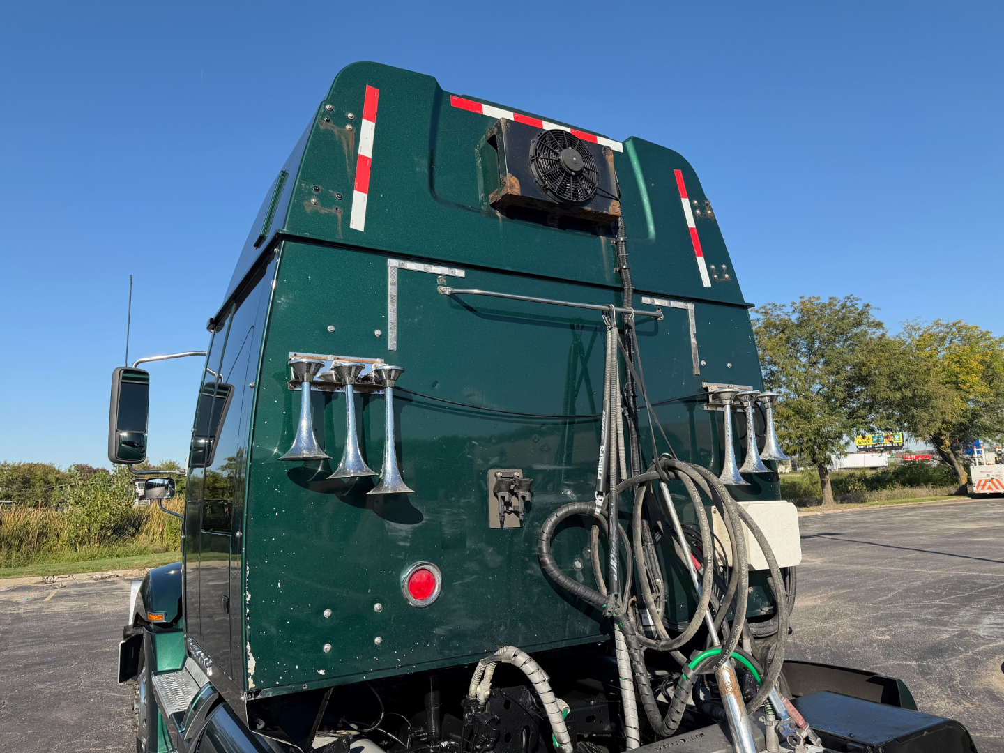 Western Star 5700XE truck sleeper cab rear view showing hoses, hoses coiled and external sirens on green body with reflective markings.