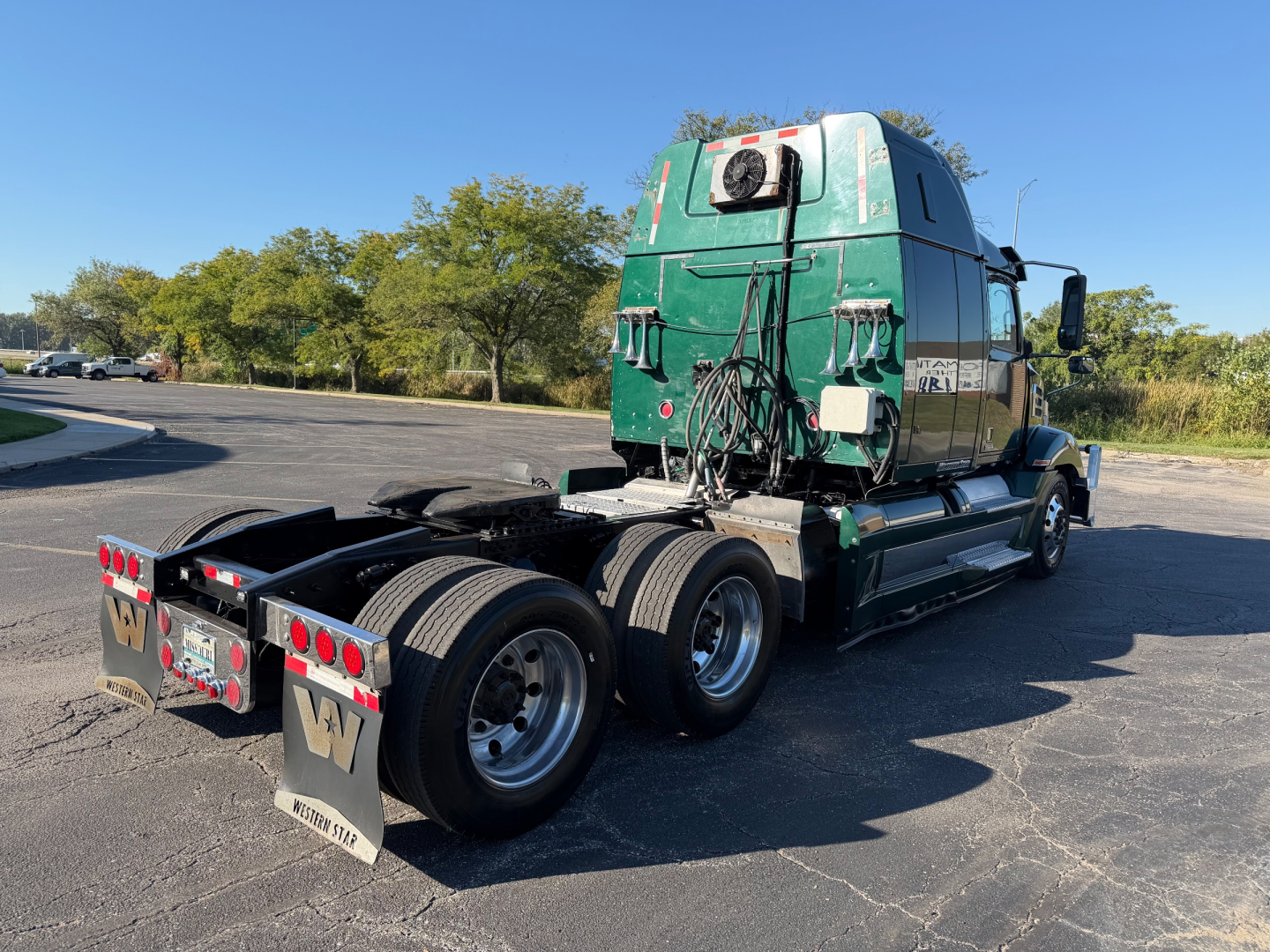 Rear view of a green 2017 Western Star 5700XE semi-truck with sleeper cab, dual rear axles, and various hoses and components on the back.