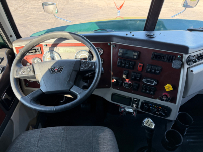 Conventional sleeper truck cab interior showing steering wheel and dashboard with gauges and control switches.