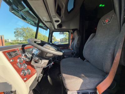 Interior cabin of a 2017 Western Star 5700XE showing steering wheel, dashboard with gauges, driver seat, and upholstery with red woodgrain trim.