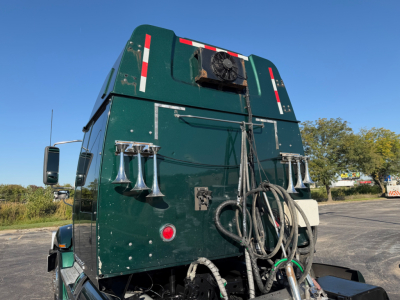Western Star 5700XE truck sleeper cab rear view showing hoses, hoses coiled and external sirens on green body with reflective markings.