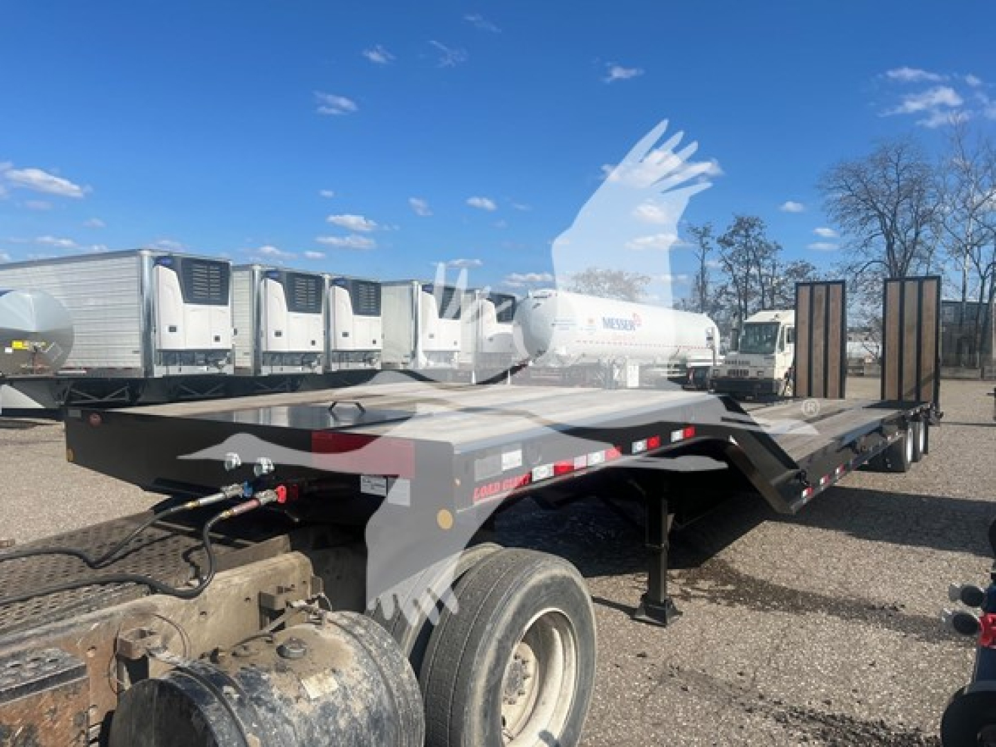 Flatbed trailer showing dual rear wheels and long deck with gooseneck hitch area visible.
