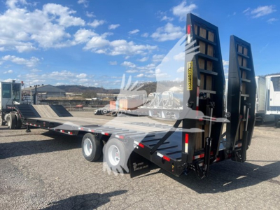Trailer deck with two rear ramps raised, black metal frame, tandem axles, in a parking lot under blue sky.