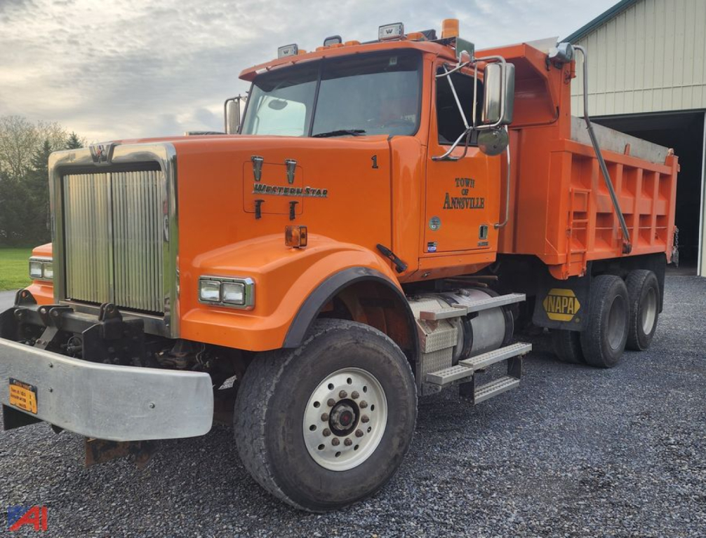 Western Star 4900 SF dump truck in orange with plow and sander, front grille and bumper visible, side lettering and dual rear wheels.