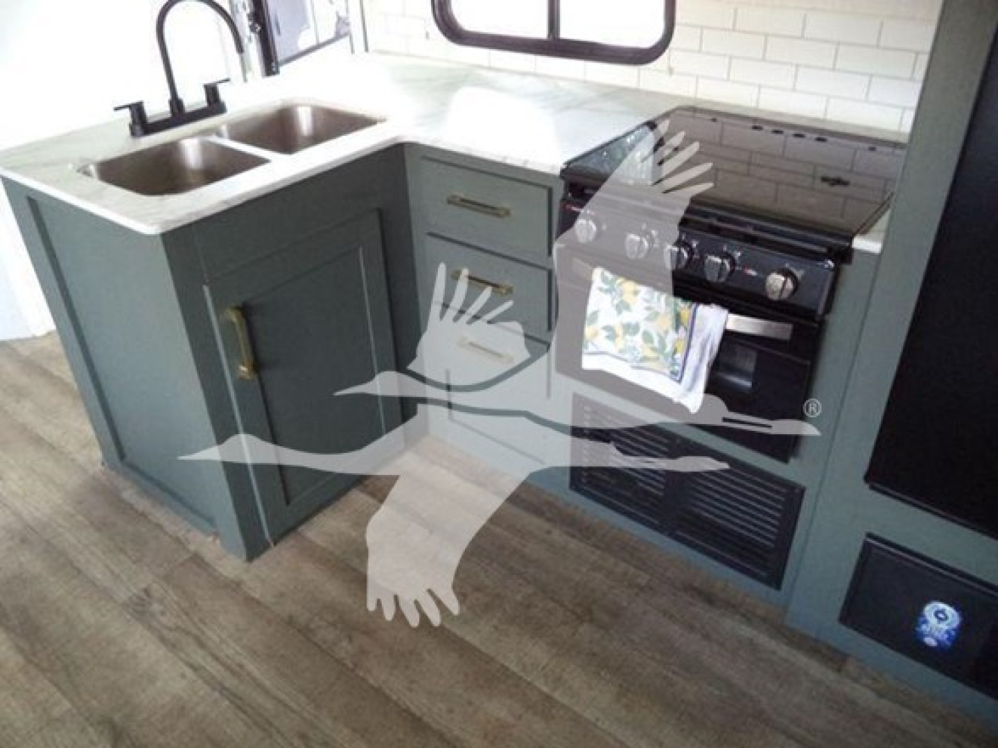 Kitchen in travel trailer showing double sink, blue cabinets, countertop, and a stove/oven on the right.