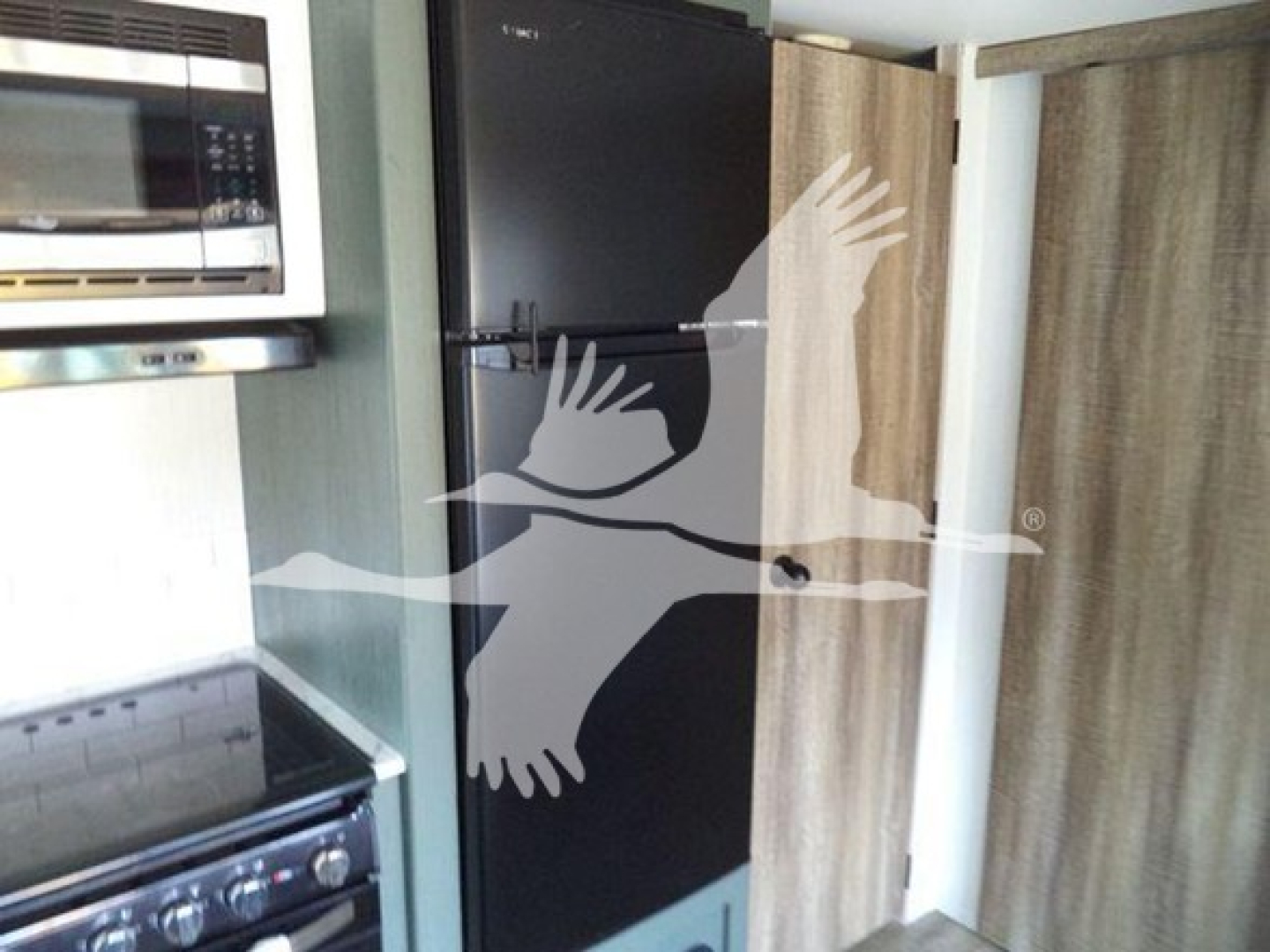 Refrigerator and microwave in a travel trailer kitchen area with a black tall fridge and wooden paneling.