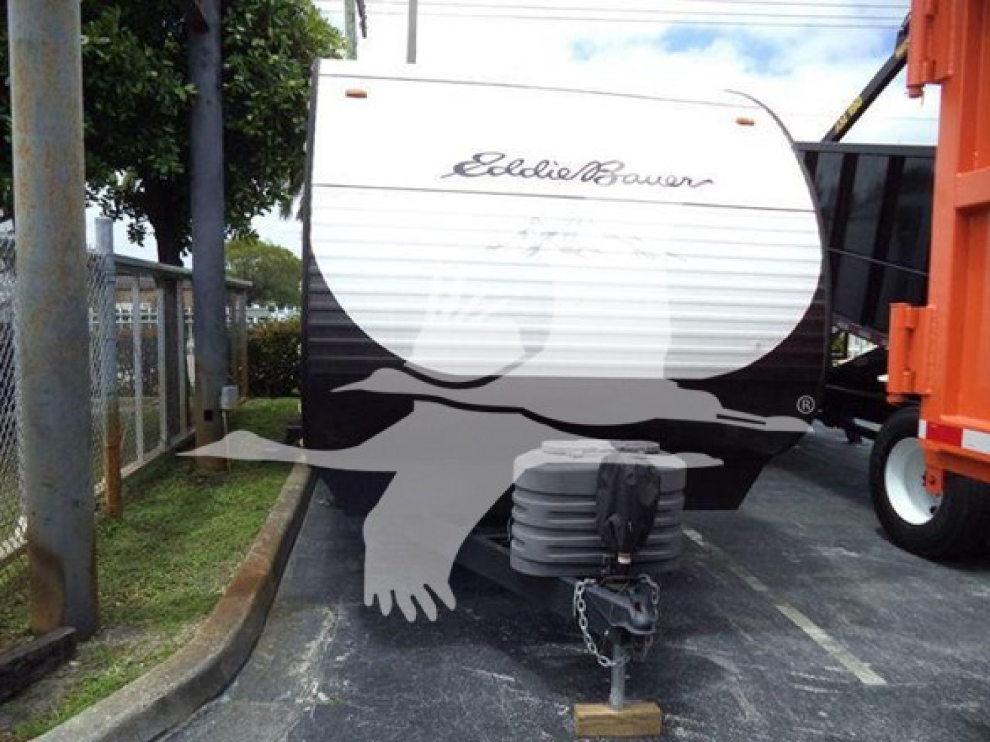 Trailer front view showing Elliott-Bauer logo on white-and-black exterior with hitch and propane tank covers in foreground