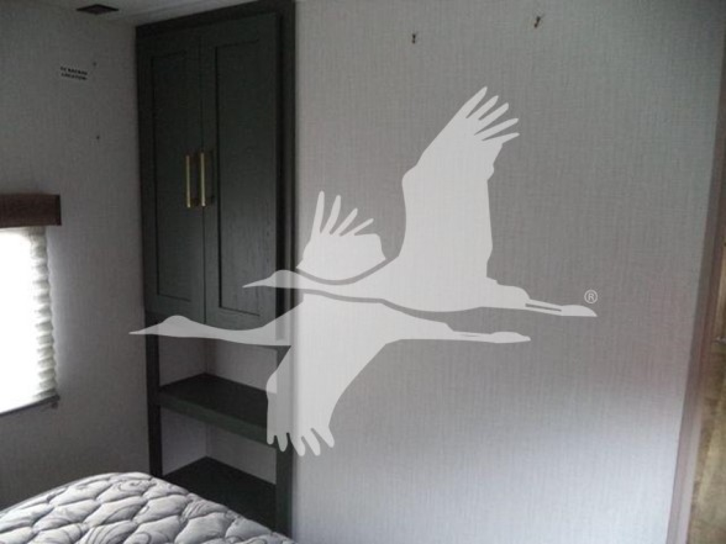 Trailer interior with a bunk, cabinets, and a shelf; large white silhouettes of geese overlay the image.