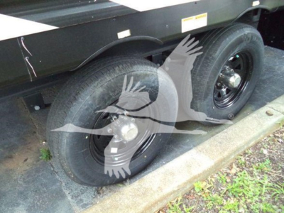 Trailer wheel area showing dual axles with black rims and tires, part of a travel trailer with a dark body and reflective decals.