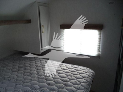 Travel trailer interior showing a bed with quilted mattress and a window with shade. No clear labels or fluid reservoirs visible.