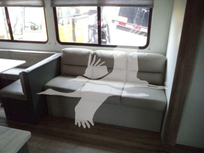 Interior of travel trailer showing a light gray sofa with storage area and windows along the wall.