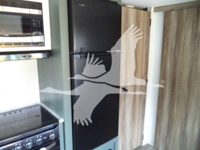 Refrigerator and microwave in a travel trailer kitchen area with a black tall fridge and wooden paneling.