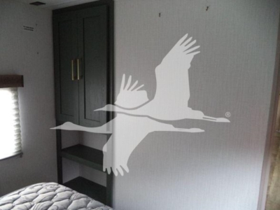 Trailer interior with a bunk, cabinets, and a shelf; large white silhouettes of geese overlay the image.