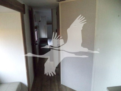 Interior trailer hallway with a tall light-colored door and a hallway leading to a kitchen area, with a large watermark of two birds in flight across the image.