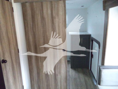 Trailer interior showing wooden cabinets, a small kitchen area with a refrigerator, and a doorway with a curtain in the travel trailer.