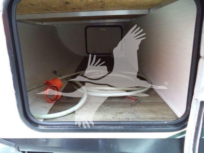 Trailer interior storage compartment showing a white hose with red coupling and utility outlet, viewed through open rear hatch