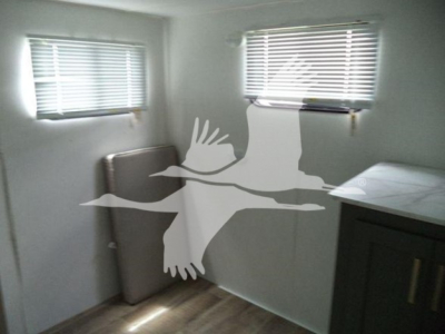 Travel trailer interior showing small windows with blinds, a cabinet, and a folded cushion/board inside.