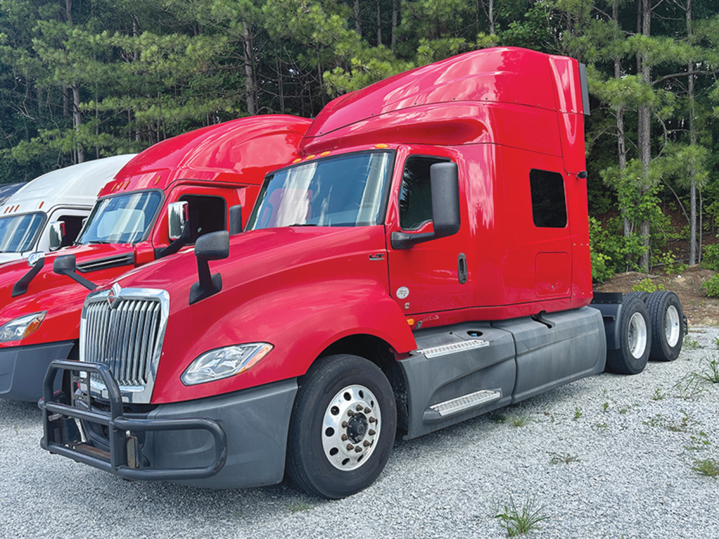 Red 2019 International LT625 sleeper truck in profile view, front bumper guard, twin rear axles, gray lower body panels, black side mirrors, chrome grille, drivers side door visible.