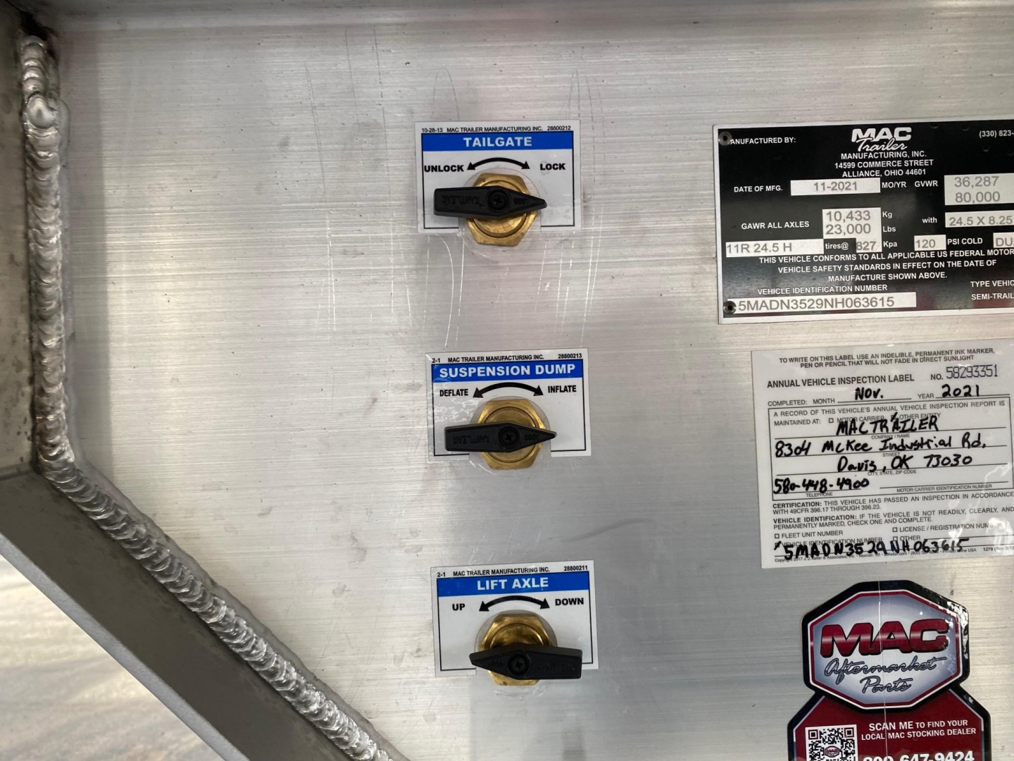 Aluminum end dump trailer interior with three blue-labeled toggle switches for tailgate, suspension dump, and lift axle, plus MAC trailer information plate.