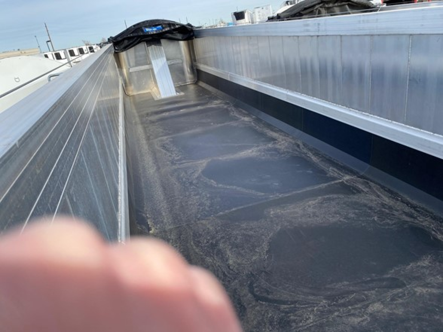 Flatbed trailer bed with metal side rails and a dark, textured deck showing wear patterns and a rear ramp area.